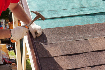 Roofer builder worker use a hammer for installing roofing shingles