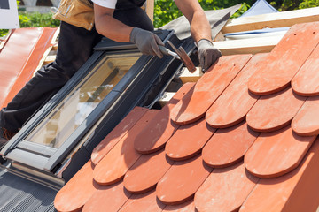 Hands of roofer laying tile on the roof. Installing natural red tile using hammer