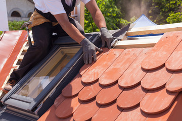 Hands of roofer laying tile on the roof. Installing natural red tile.