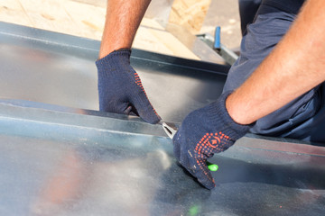Roofer builder worker finishing folding a metal sheet using special pliers with a large flat grip