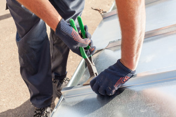 Roofer builder worker finishing folding a metal sheet using special pliers with a large flat grip - obrazy, fototapety, plakaty