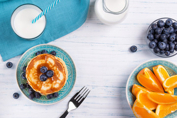Stack of pancakes with fresh blueberry, honey, milk and orange slices, healthy breakfast concept,...