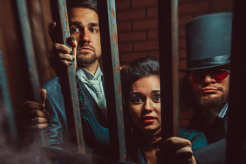 Two gentlemen and a lady behind bars in the prison.
