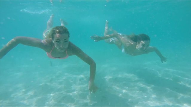 women swimming underwater in turquoise water
