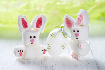 Funny marshmallow rabbits with Easter egg, sweet bunnies on a green background