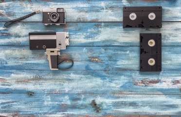 Video and photo cameras, audio cassettes, VHS video tapes on a blue old vintage background. Photographed in retro style