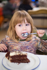 Three years old blonde cute caucasian child with knitted sweater licking spoon eating chocolate...