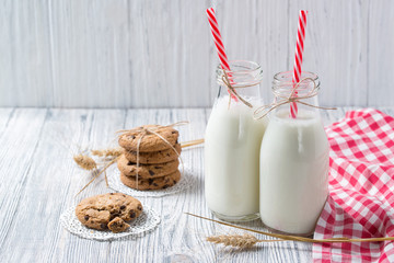 Bottles of milk and chocolate chip cookies on wooden background