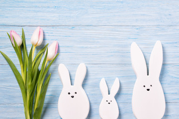 Easter background with white rabbits and pink tulips, blue wooden background, top view