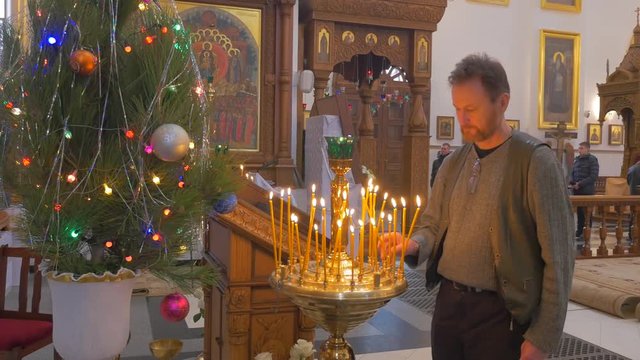 a Religious Man Lights His Candle Up, and Installs This Candle on a Candlestick With a Lot of Candles, While Standing Before Some Icon in Orthodox Church