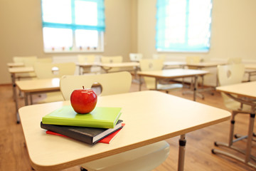 Stack of books and apple on desk at classroom