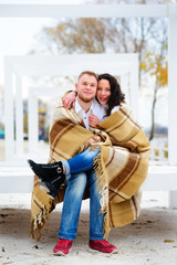 Young couple embracing and covered with a warm blanket sitting o