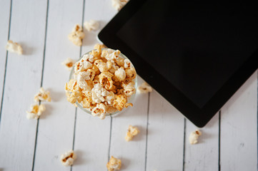 black tablet touch computer gadget with popcorn on white wooden background.