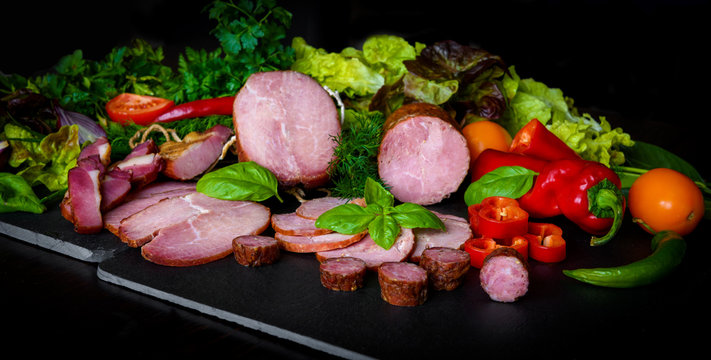 Assorted meat products: ham and sausages with herbs and vegetables