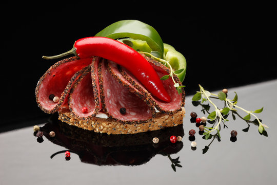Salami sandwich with cilli and paprika. On black reflective background