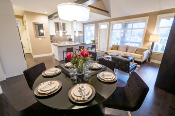 Modern round dining room table set for dinner in a luxury  house, with a kitchen in the background. Interior design.