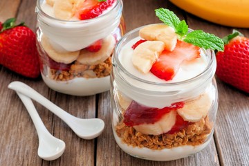 Strawberry and banana parfaits in mason jars, scene on a rustic wood background