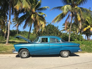 Broken down Cuban car on the side of a road with Palm trees