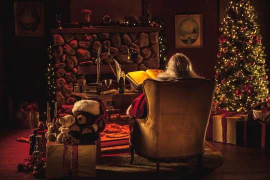 A view from behind of Santa working at his desk in a Christmas-decorated room