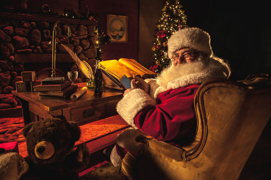 Santa Claus looks back over his shoulder and smiles, showing off his smartphone.