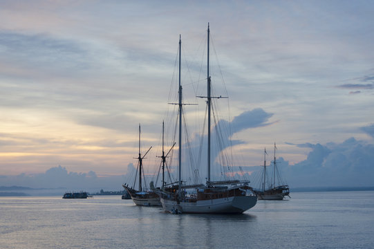 Boats Anchored in Sorong Harbor at Sunrise. Traditional phinisi schooners at anchor in Sarong Harbor. West Papua, Raja Ampat, Indonesia.