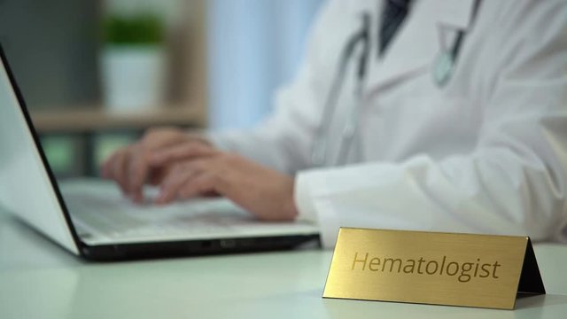 Attentive male hematologist typing medical report on laptop, working in office