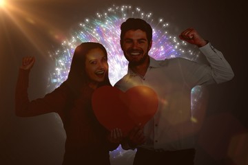 Composite image of cheerful couple holding paper heart