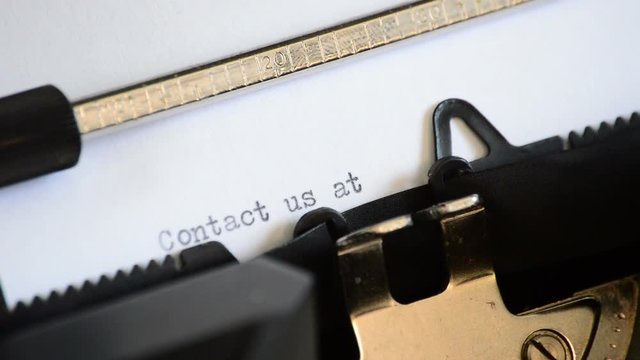 Typing the expression Contact us at: with an old manual typewriter