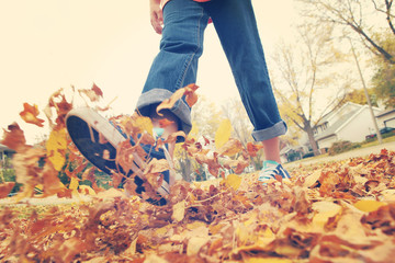 Child walking and kicking fall leaves. Focus on leaves in center