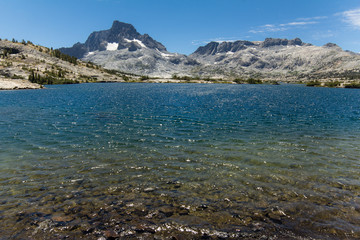 Tall granite peak rises over a blue alpine lake in the high sierra