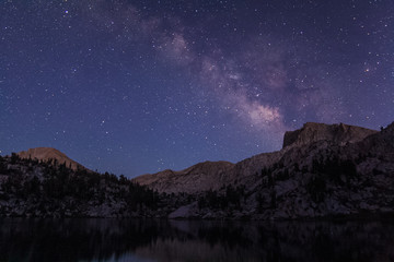 Naklejka premium Milky way rises over a granite bluff at the Lake of the Lone Indian in the high sierra