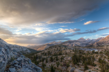 Fototapeta na wymiar Sunset over an alpine basin with lake and pine trees surrounded by tall bare granite peaks in California