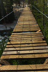An old wooden suspension bridge with broken slats hangs over a river near the Rae Lakes in California's high sierra