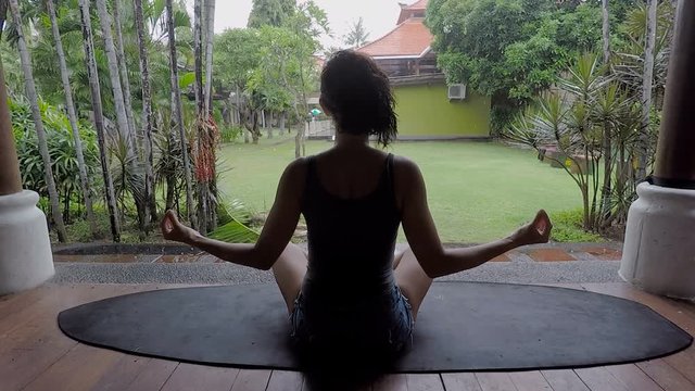 Rainy day on the island of Bali. The girl meditates in a pose of the yogi. The brunette relaxes and has a rest. Bali the real Mecca for persons interested to reunite with the magic nature