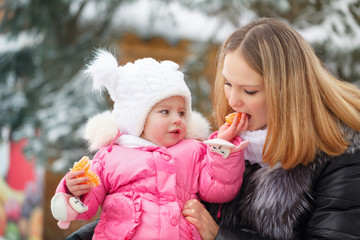 Obraz premium Mother holds daughter on hands outdoors. Little girl feeding mother mandarin. Family walk in a winter park. Family happiness.