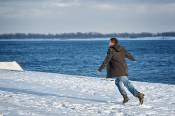 Fototapeta na wymiar Man runs along the waterfront. He is dressed in coat, scarf, jeans and gloves. Winter.