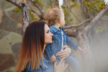 Naklejka premium Mother and daughter in a spring park. Mother daughter landed on her shoulder. Girls dressed in denim jackets. Spring mood. Family time.