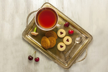 Vintage tray with tea cup, biscuits, cherries, and flower