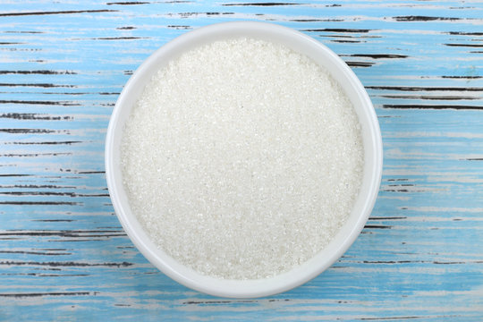 White sugar in white bowl over wooden background