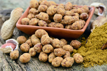 Coated Peanuts mit Curry auf Holztisch, Nahaufnahme, Food Styling 