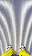Top View of a Feet in snowboard boots on newly groomed snow on ski slope on a sunny winter day.