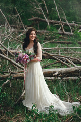 Beautiful bride in the forest with a large bouquet of different flowers. Boho style