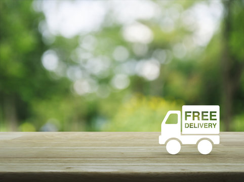 Free delivery truck icon on wooden table over blur green tree background, Transportation business concept