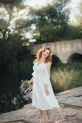 Beautiful bride with a big bouquet of different flowers posing on nature background