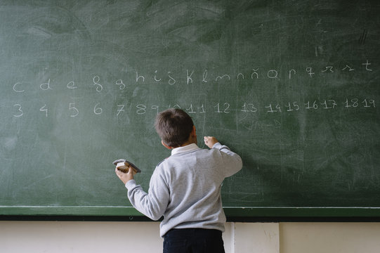 Rear view of boy writing on blackboard