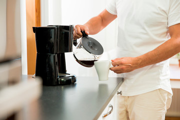 Man in the kitchen pouring a mug of hot filtered coffee from a glass pot. Having breakfast in the morning - Powered by Adobe