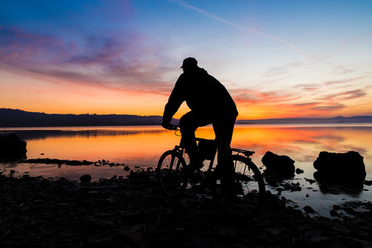 Silhouette of a mountain bike and of a cyclist who is watching the sunrise over the lake (lake Varese - Varese, Italy)