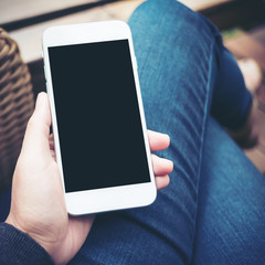 Mockup image of hand holding white mobile phone with blank black screen on thigh 