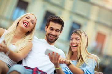 Three friends sitting on a bench and looking the phone on a sunny day