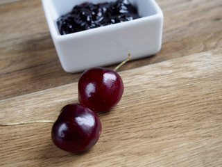 Cherry jam unfocused with two cherries on wood background